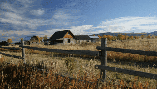 Cabin in a field next to a wooden fence.