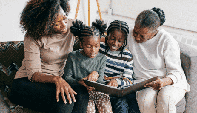 A mother, grandmother and granddaughters reading about family traditions together on a sofa.