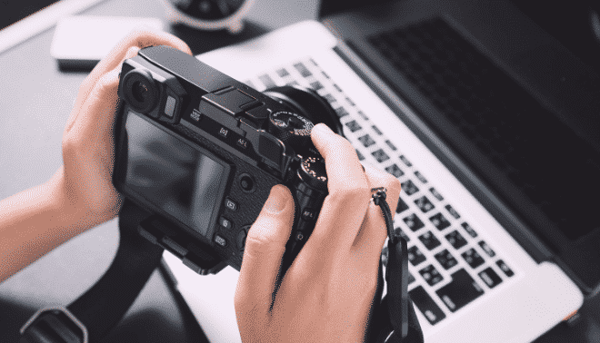 Person holding a digital camera next to a laptop.