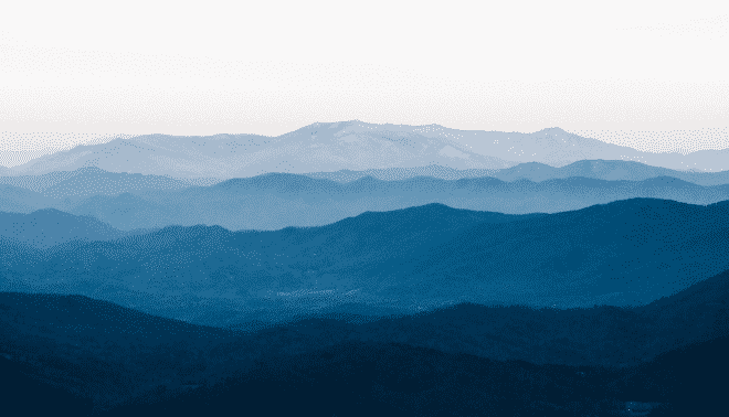 A scenic view of distant mountains under a clear sky, with overlapping layers of ridges creating a sense of depth.