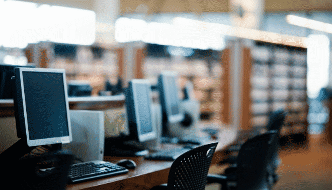 Computers at a library with shelves in the background.