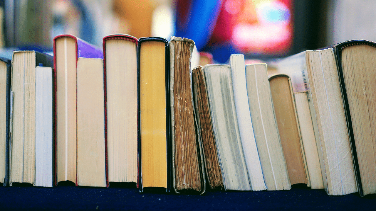 A row of various books with worn and colorful spines placed upright on a dark surface, with blurred background.