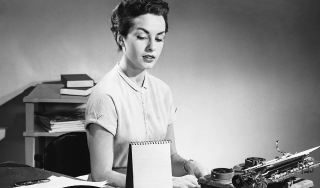 Black and white photo of a woman typing at a desk.