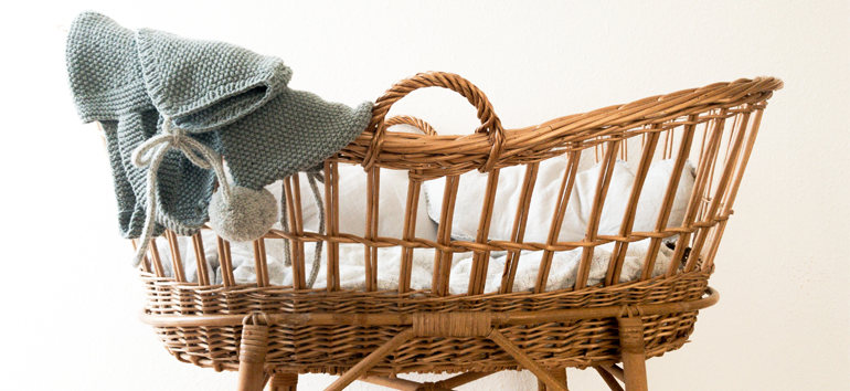 baby covered with pink blanket in brown woven basket with brown