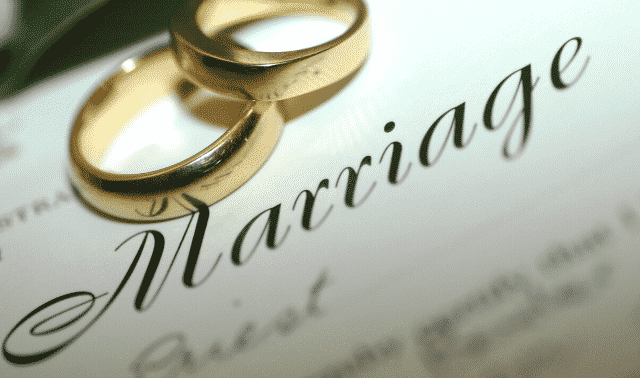 Two gold wedding rings placed on a document with the word "Marriage" written in elegant script.