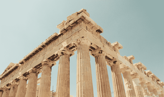 The image shows the Parthenon, an ancient Greek temple with tall columns and a partially intact pediment, set against a clear blue sky.