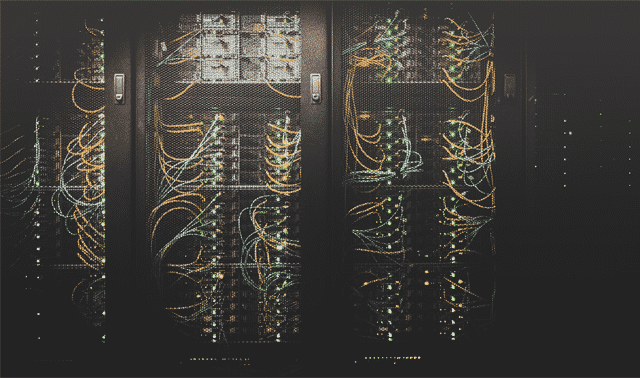 A server room with racks filled with numerous interconnected network cables and hardware components. The cables are neatly organized and connected to various ports.