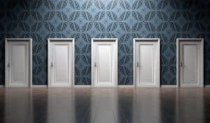 A row of five closed white doors are evenly spaced along a patterned dark blue wallpapered wall above a shiny wooden floor.