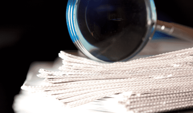 Close-up of a magnifying glass examining a stack of white braided cords on a reflective surface.