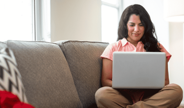 Woman sitting on couch with laptop computer, looking at Hispanic genealogy websites.