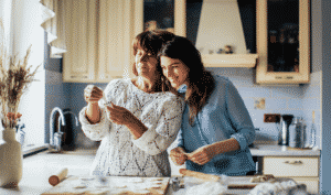 Two women, one older and one younger, are in a kitchen making dumplings together. The table is covered with dumpling wrappers and fillings. They appear to be enjoying the activity.