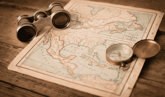 A map of North and Central America is spread on a wooden surface, accompanied by a pair of binoculars and a pocket watch.