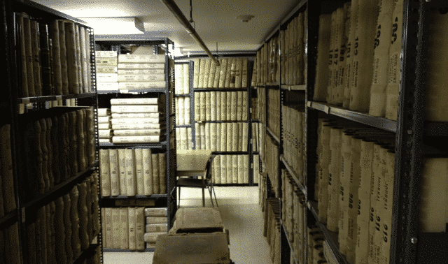 A dimly lit basement containing several binders of records on metal shelves