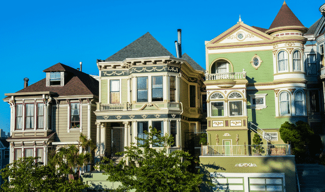 A row of three colorful Victorian-style houses with ornate details and balconies under a clear blue sky.