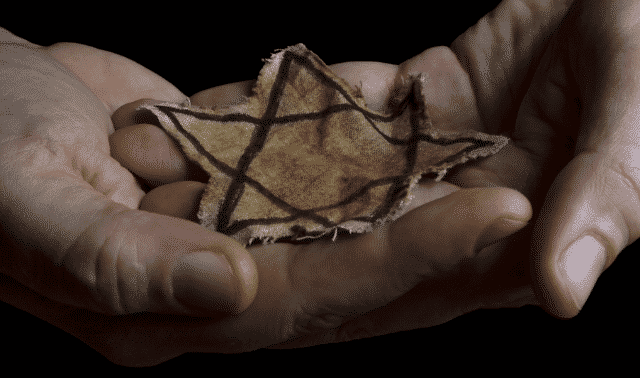 Pair of hands cradling a yellow fabric Star of David from the Jewish Holocaust