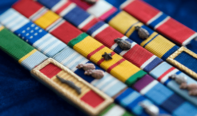 Close-up of military ribbons and medals arranged neatly on a dark blue fabric background.