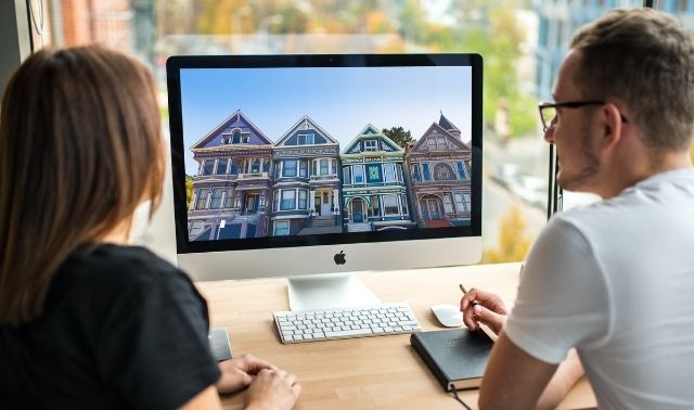 A man and woman sitting at a desktop computer with old houses on the screen and researching house histories