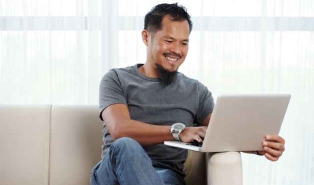 Man sitting on couch holding laptop while researching Filipino genealogy websites