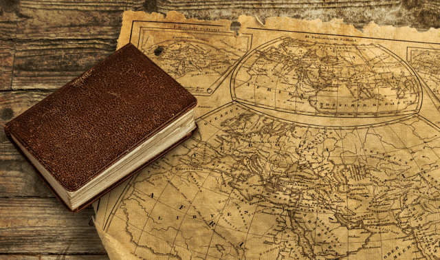 A vintage book lies next to an old, detailed map on a wooden surface.