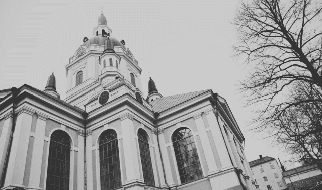 Black and white photo of a large, ornate church with domes and tall windows, framed by leafless trees.