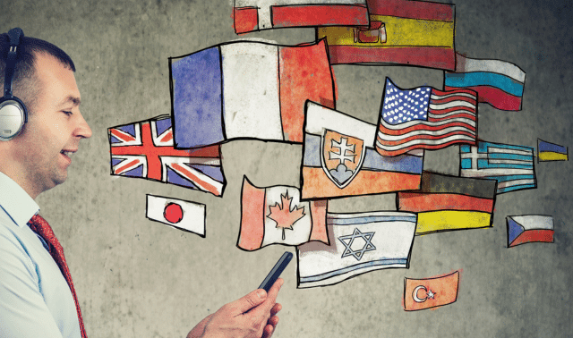 A man wearing headphones looks at his phone, with illustrated flags from various countries floating between him and the gray wall background.