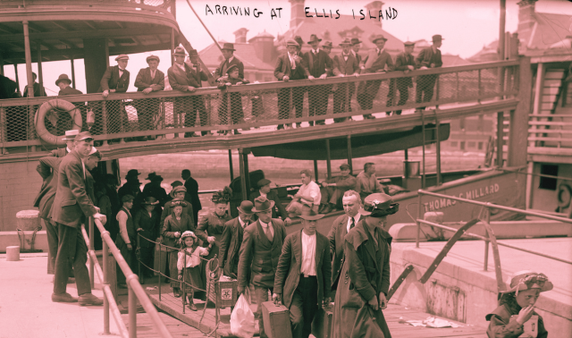 Men and women in early 20th-century attire step off a boat carrying luggage