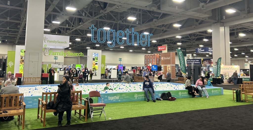 People sit on benches and relax by a ball pit in a convention center filled with booths and banners, with a large "together" sign hanging above.